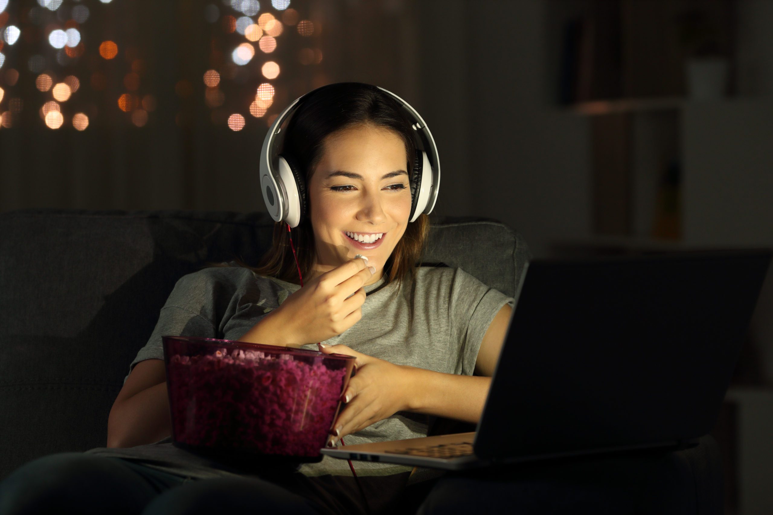 Woman watching a video and eating popcorn on the couch with headphones on